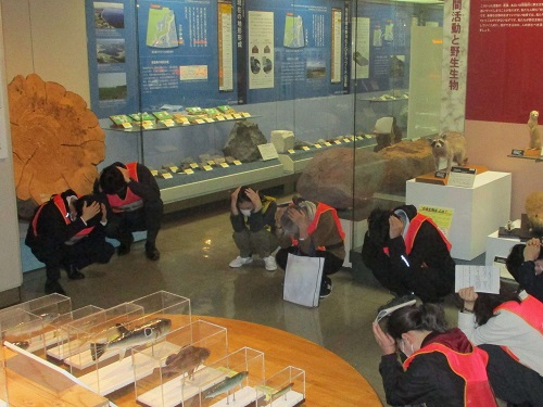 職員と来館者が展示室で避難姿勢をとる様子の写真　